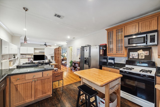 kitchen featuring ornamental molding, appliances with stainless steel finishes, pendant lighting, dark wood-type flooring, and dark stone countertops