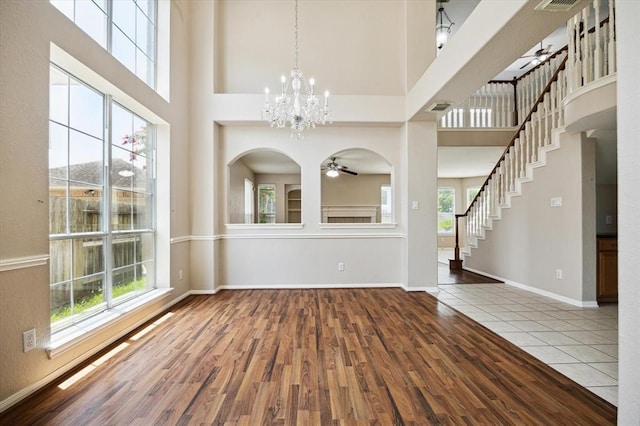 unfurnished dining area featuring ceiling fan with notable chandelier, a towering ceiling, and hardwood / wood-style flooring