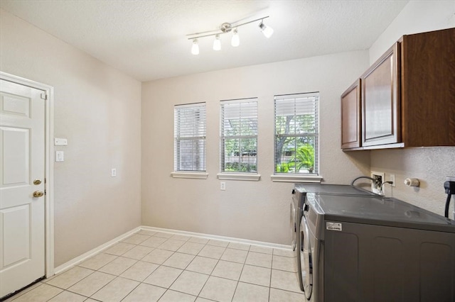 clothes washing area featuring washer and dryer, light tile patterned flooring, cabinets, and a textured ceiling