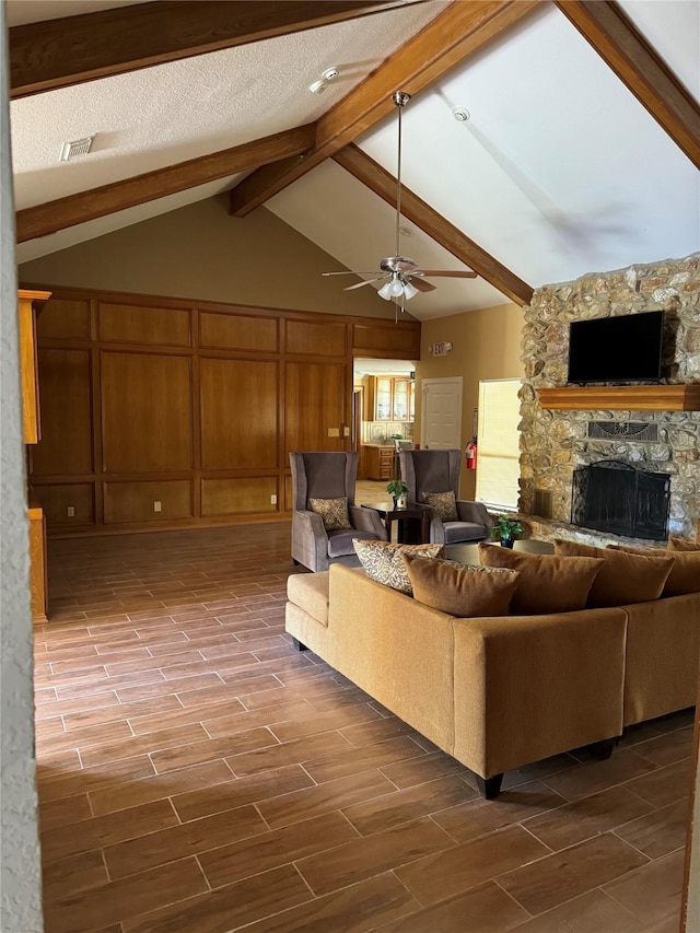 living room featuring hardwood / wood-style floors, vaulted ceiling with beams, ceiling fan, and a stone fireplace