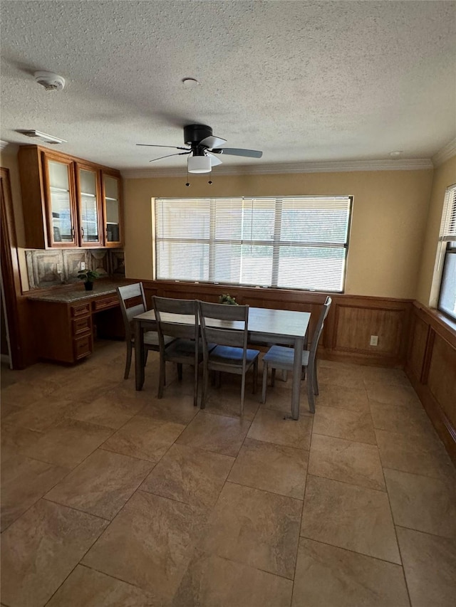 dining space with tile patterned floors, ceiling fan, ornamental molding, and a textured ceiling