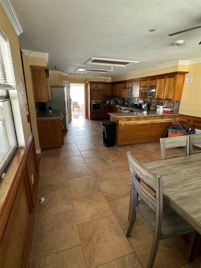 kitchen featuring stainless steel refrigerator, kitchen peninsula, crown molding, decorative backsplash, and light tile patterned flooring