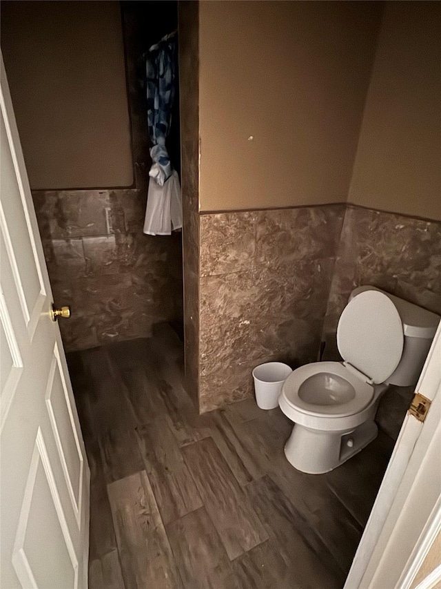 bathroom with wood-type flooring, tile walls, and toilet