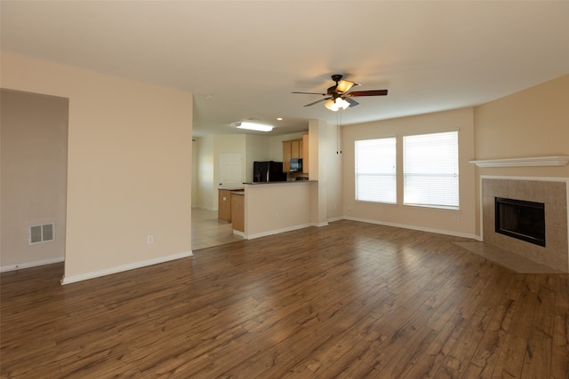 unfurnished living room with a tile fireplace, dark hardwood / wood-style floors, and ceiling fan