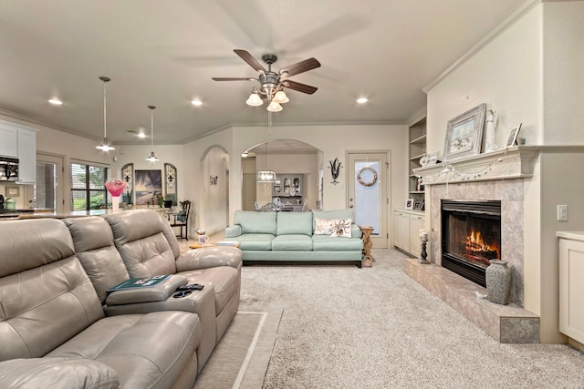 carpeted living room featuring built in features, ornamental molding, a tile fireplace, and ceiling fan