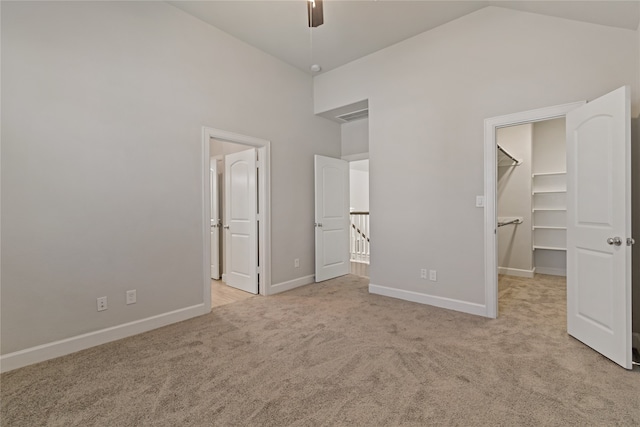 unfurnished bedroom with light carpet, ceiling fan, a spacious closet, a closet, and vaulted ceiling