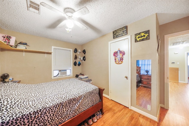 bedroom featuring cooling unit, a textured ceiling, ceiling fan, and light hardwood / wood-style flooring