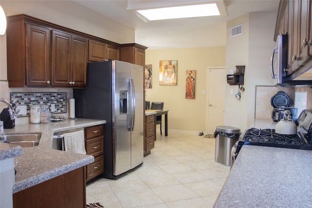 kitchen with dark brown cabinetry, sink, tasteful backsplash, light tile patterned floors, and appliances with stainless steel finishes