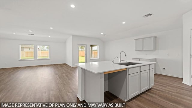 kitchen featuring gray cabinetry, sink, dark wood-type flooring, an island with sink, and vaulted ceiling