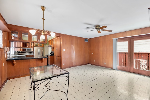 kitchen featuring stainless steel appliances, wood walls, decorative light fixtures, and kitchen peninsula