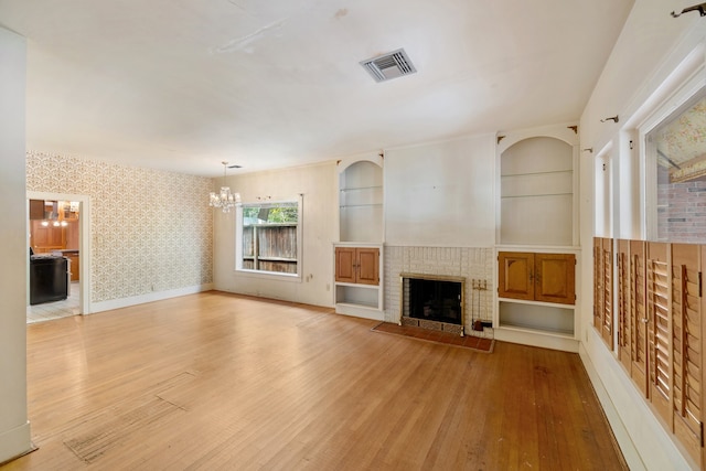 unfurnished living room featuring built in features, a chandelier, hardwood / wood-style floors, and a fireplace