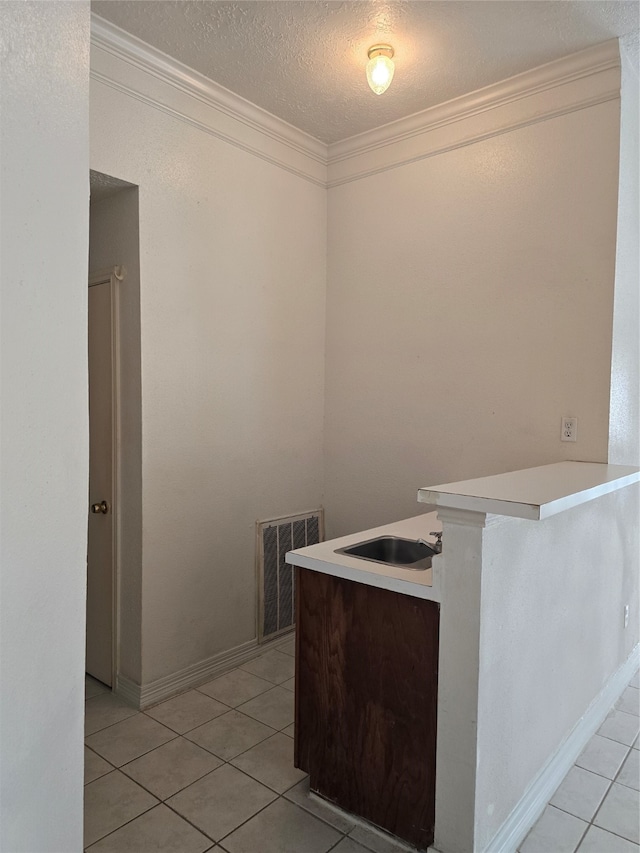 kitchen with kitchen peninsula, a textured ceiling, light tile patterned floors, sink, and ornamental molding