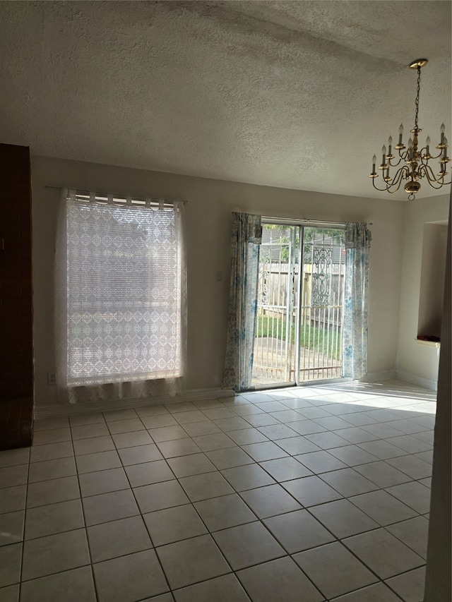 tiled empty room featuring a textured ceiling and a notable chandelier