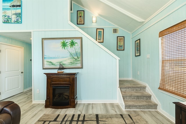 stairway featuring wood-type flooring, wooden walls, lofted ceiling with beams, and ornamental molding