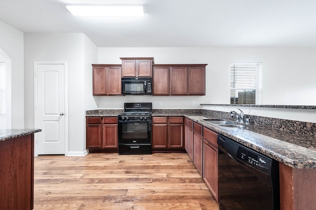 kitchen with light wood-type flooring, dark stone countertops, sink, and black appliances