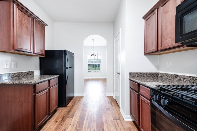 kitchen with dark stone countertops, a chandelier, black appliances, and light hardwood / wood-style flooring