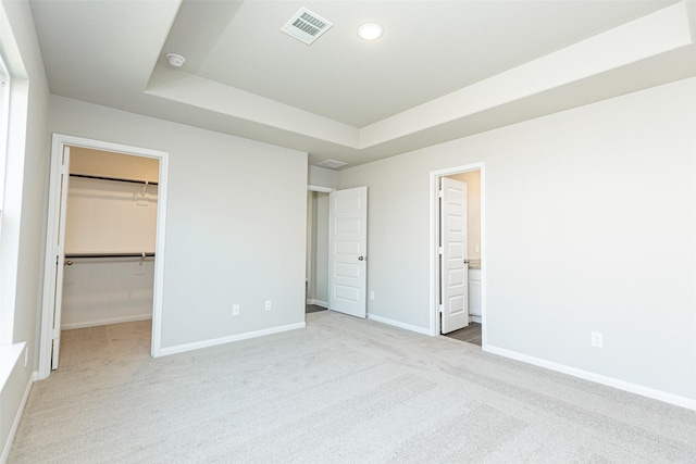 unfurnished bedroom with carpet floors, a closet, a spacious closet, and ensuite bath