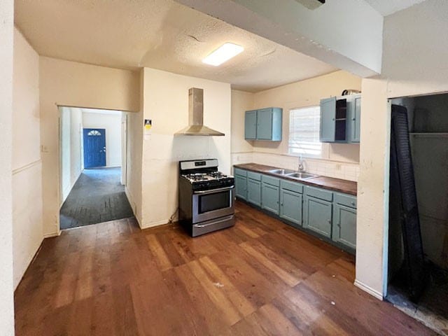 kitchen featuring dark hardwood / wood-style flooring, butcher block counters, stainless steel range with gas stovetop, sink, and wall chimney range hood