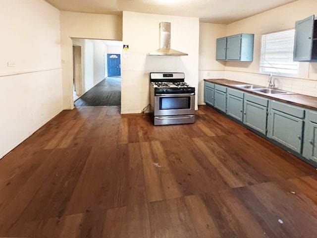 kitchen with wall chimney range hood, wood counters, sink, dark wood-type flooring, and stainless steel range with gas stovetop