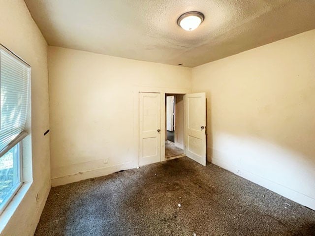 spare room featuring a textured ceiling and dark colored carpet