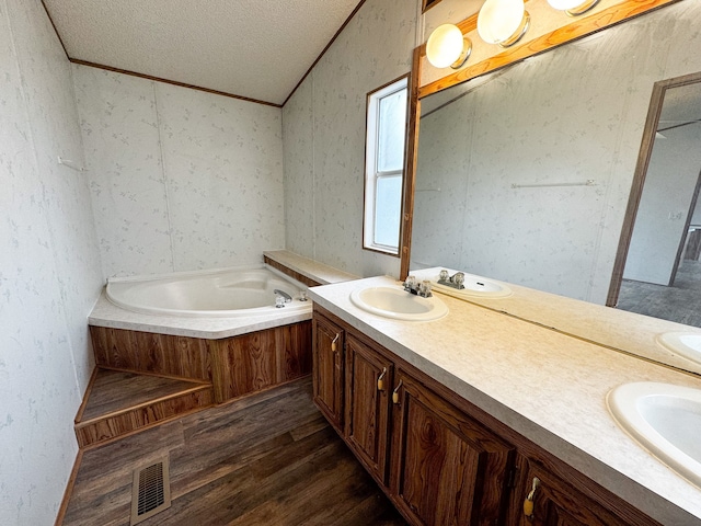 bathroom featuring hardwood / wood-style floors, a textured ceiling, ornamental molding, vanity, and a tub to relax in