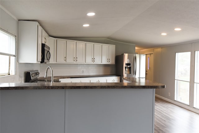 kitchen with stainless steel appliances, vaulted ceiling, backsplash, white cabinetry, and light wood-type flooring