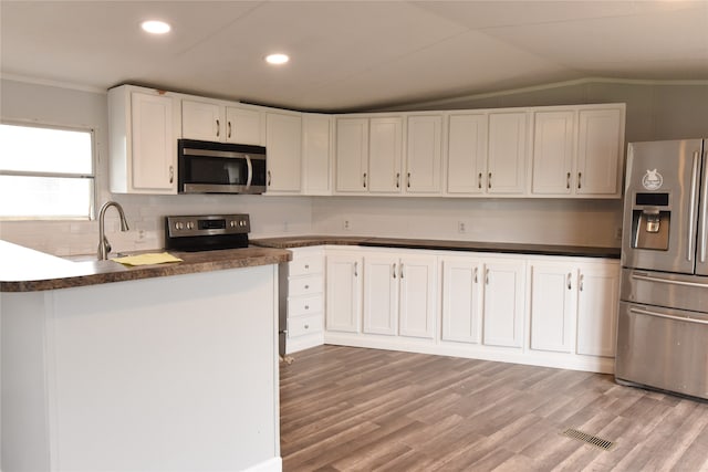 kitchen featuring stainless steel appliances, lofted ceiling, backsplash, white cabinetry, and light hardwood / wood-style flooring