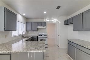 kitchen with kitchen peninsula, gray cabinetry, light stone counters, and white range oven