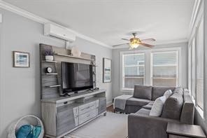 living room featuring ornamental molding, an AC wall unit, and ceiling fan