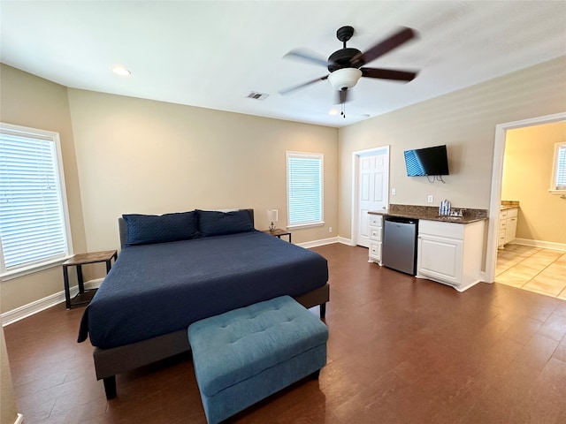 bedroom with connected bathroom, multiple windows, dark wood-type flooring, and ceiling fan