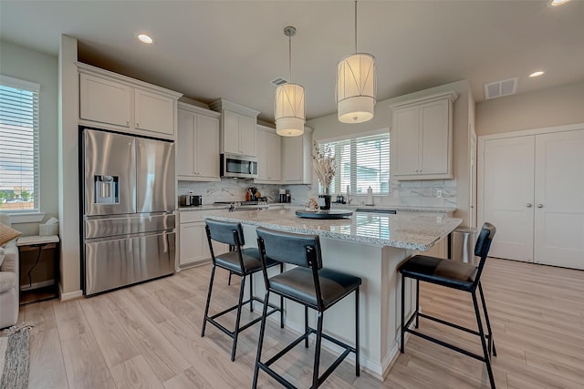 kitchen with tasteful backsplash, hanging light fixtures, white cabinetry, and stainless steel appliances