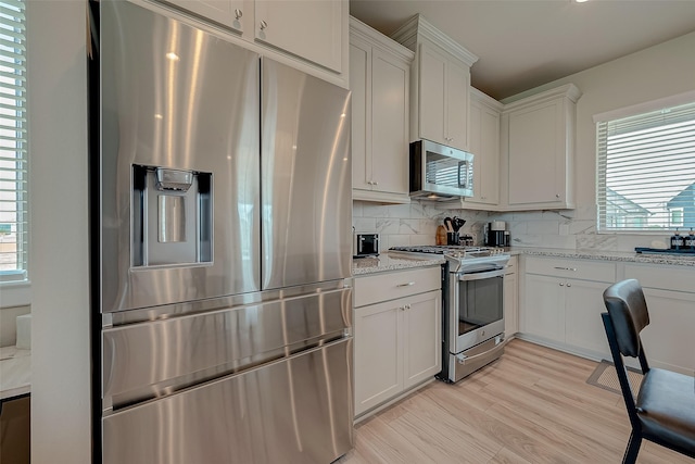 7659 Green Bulrush Way, Katy, TX 77493 - kitchen with stainless steel appliances, backsplash, light stone countertops, light wood finished floors, and white cabinetry