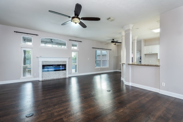 unfurnished living room featuring a fireplace, dark hardwood / wood-style flooring, ceiling fan, and ornate columns