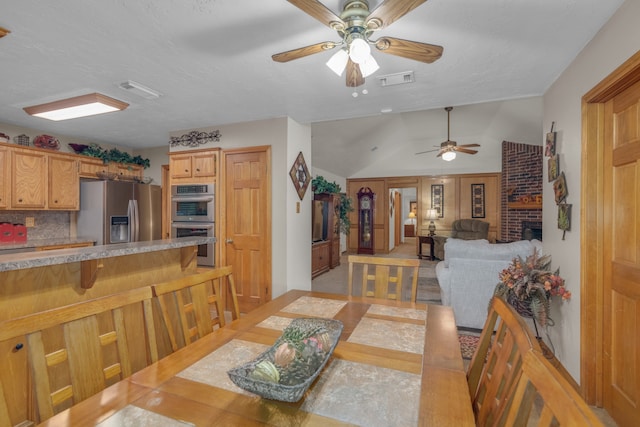 dining area with a fireplace, light tile patterned flooring, ceiling fan, and vaulted ceiling