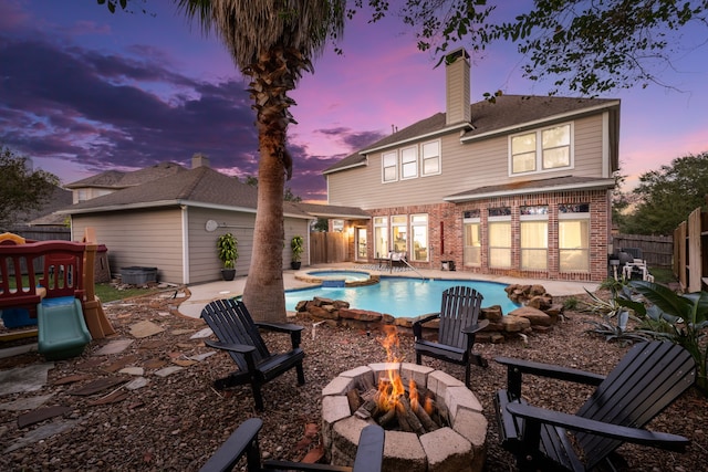 back house at dusk featuring a fire pit, a pool with hot tub, and a patio area