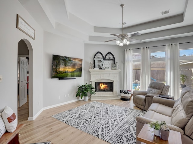 living room featuring light wood-type flooring, a tray ceiling, ceiling fan, and a healthy amount of sunlight