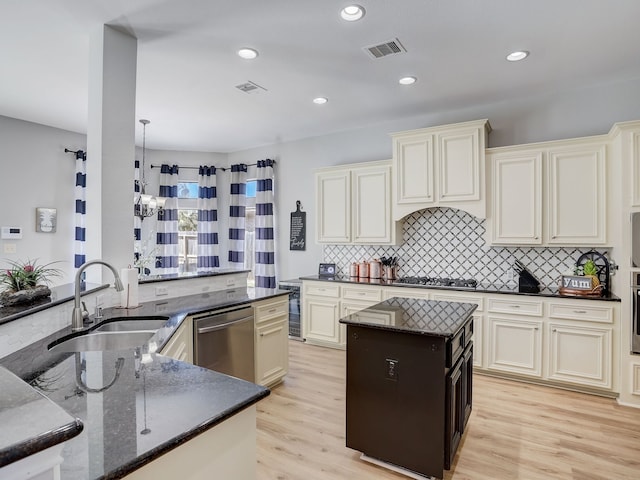 kitchen with sink, appliances with stainless steel finishes, dark stone countertops, cream cabinetry, and light wood-type flooring