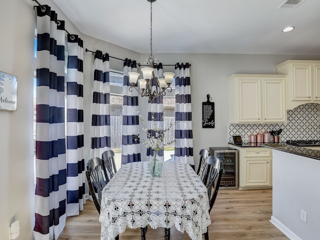 dining space with light hardwood / wood-style flooring, beverage cooler, and an inviting chandelier