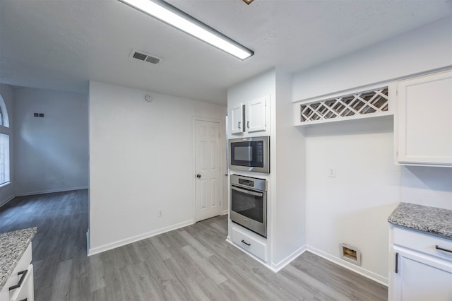 kitchen with white cabinetry, appliances with stainless steel finishes, light stone counters, and light hardwood / wood-style floors