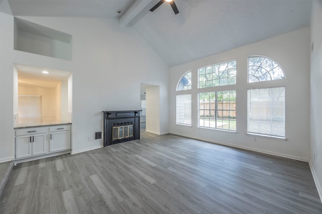 unfurnished living room featuring high vaulted ceiling, beamed ceiling, hardwood / wood-style flooring, and ceiling fan