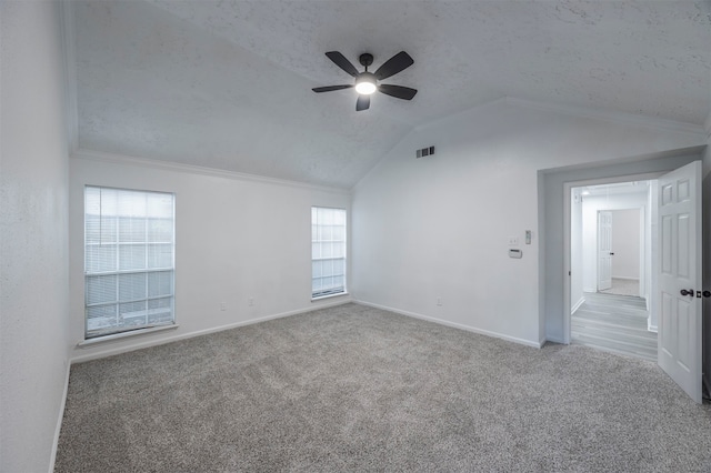 carpeted empty room with a textured ceiling, lofted ceiling, a healthy amount of sunlight, and ceiling fan