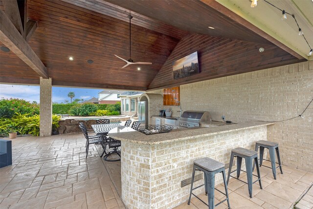 view of patio / terrace featuring ceiling fan, area for grilling, exterior bar, and an outdoor kitchen