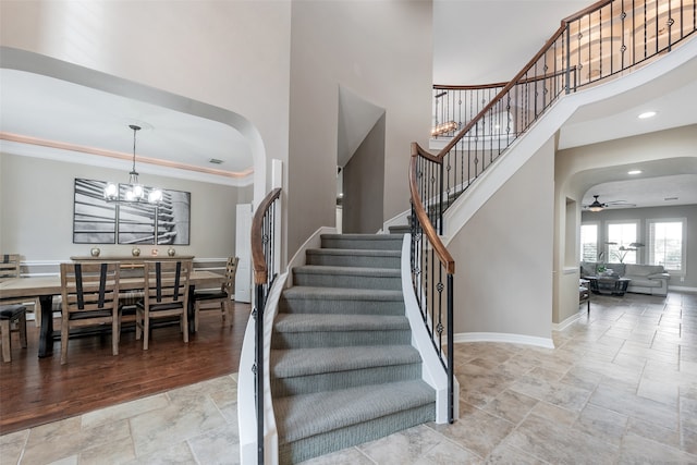 staircase with a towering ceiling, wood-type flooring, ceiling fan with notable chandelier, and crown molding