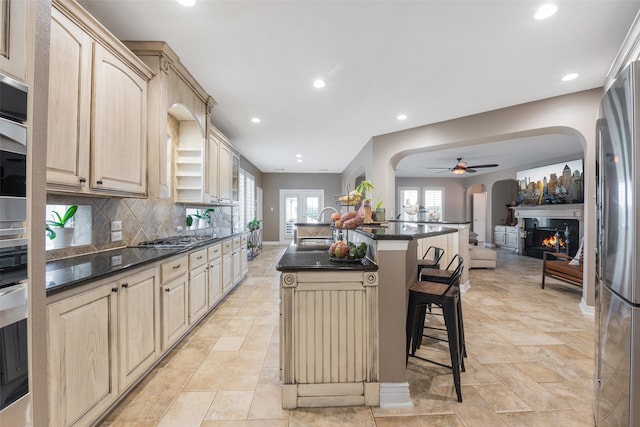 kitchen with decorative backsplash, light brown cabinetry, appliances with stainless steel finishes, a kitchen island, and a breakfast bar area