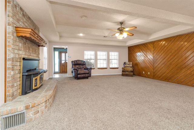 living area with ceiling fan, a textured ceiling, a tray ceiling, and wood walls