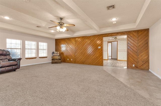 unfurnished living room with wooden walls, ceiling fan, light colored carpet, a textured ceiling, and beamed ceiling