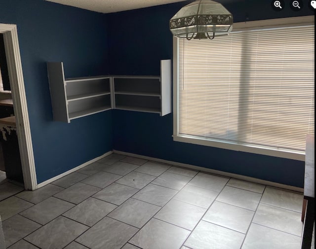 tiled empty room with a textured ceiling and a chandelier