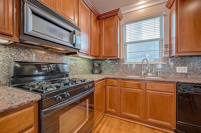 kitchen with black appliances, light stone counters, decorative backsplash, sink, and light hardwood / wood-style floors