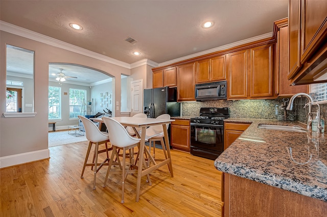 kitchen with stone countertops, sink, black appliances, ornamental molding, and light wood-type flooring