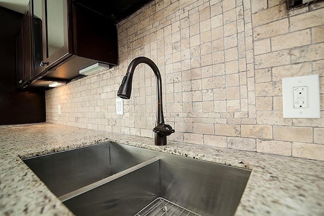 kitchen featuring light stone countertops, dark brown cabinets, tasteful backsplash, and sink